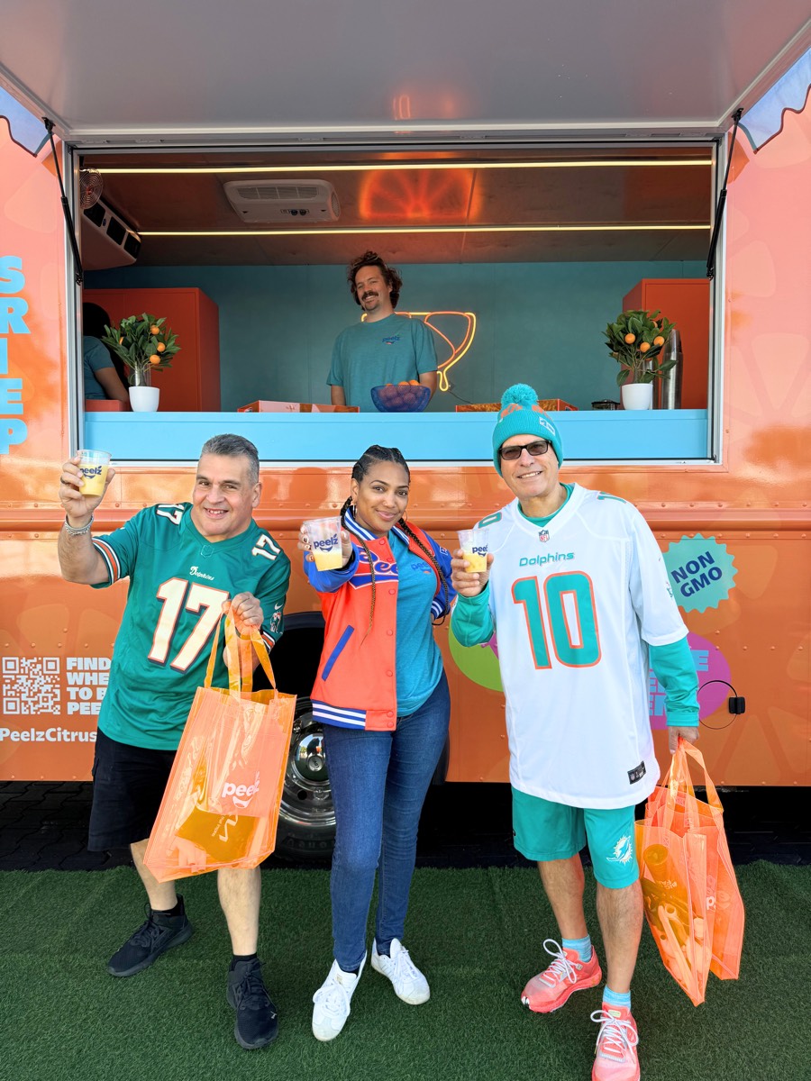 Three fans in Dolphins jerseys holding Peelz bags at the truck